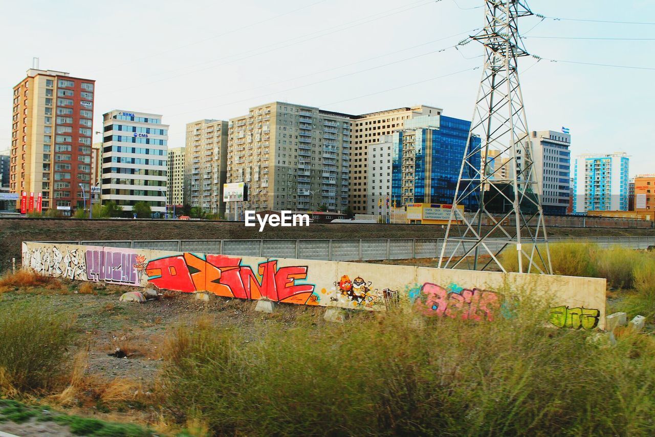 Graffiti on wall by electricity pylon with buildings seen in background