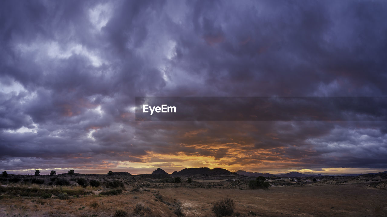 SCENIC VIEW OF DRAMATIC SKY OVER LANDSCAPE AGAINST CLOUDY SUNSET