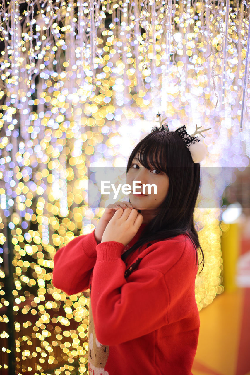 portrait of young woman standing against illuminated christmas