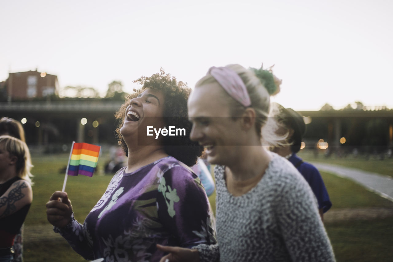 Cheerful transgender woman holding rainbow flag while enjoying with non-binary friend at gay pride parade