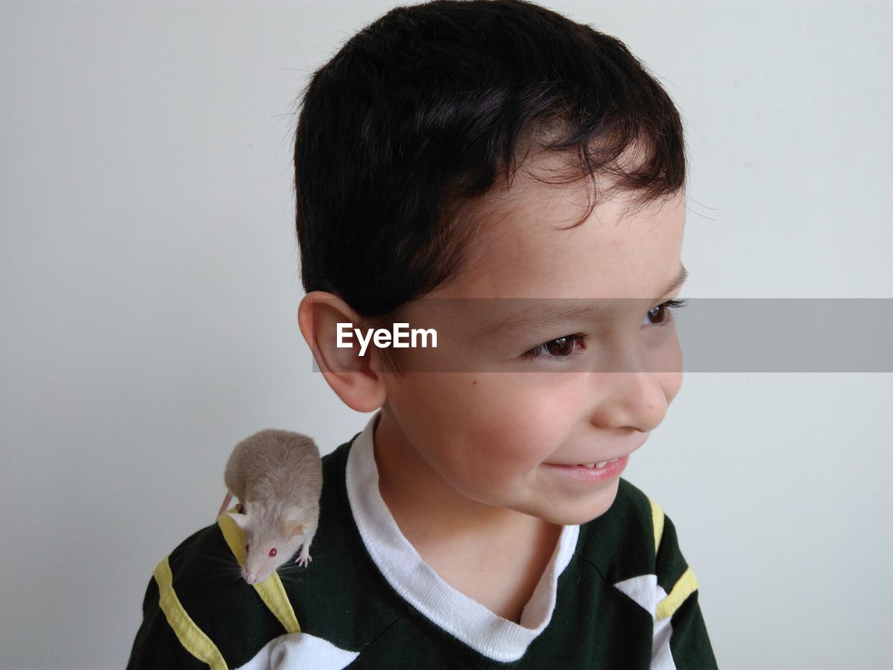 Close-up of cute happy boy with mouse on shoulder against wall