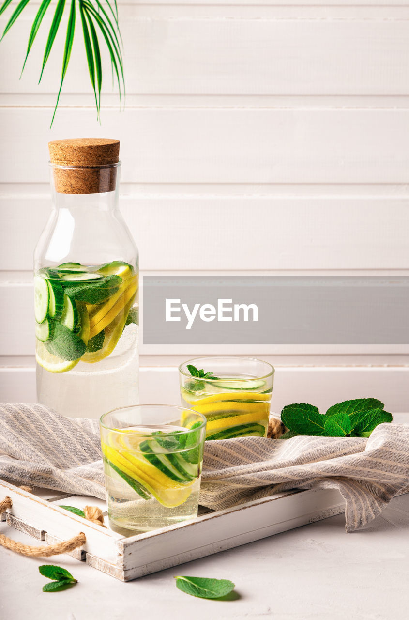 Sassy water for detox infused with lemon, cucumber and mint in glasses at white wooden tray. 