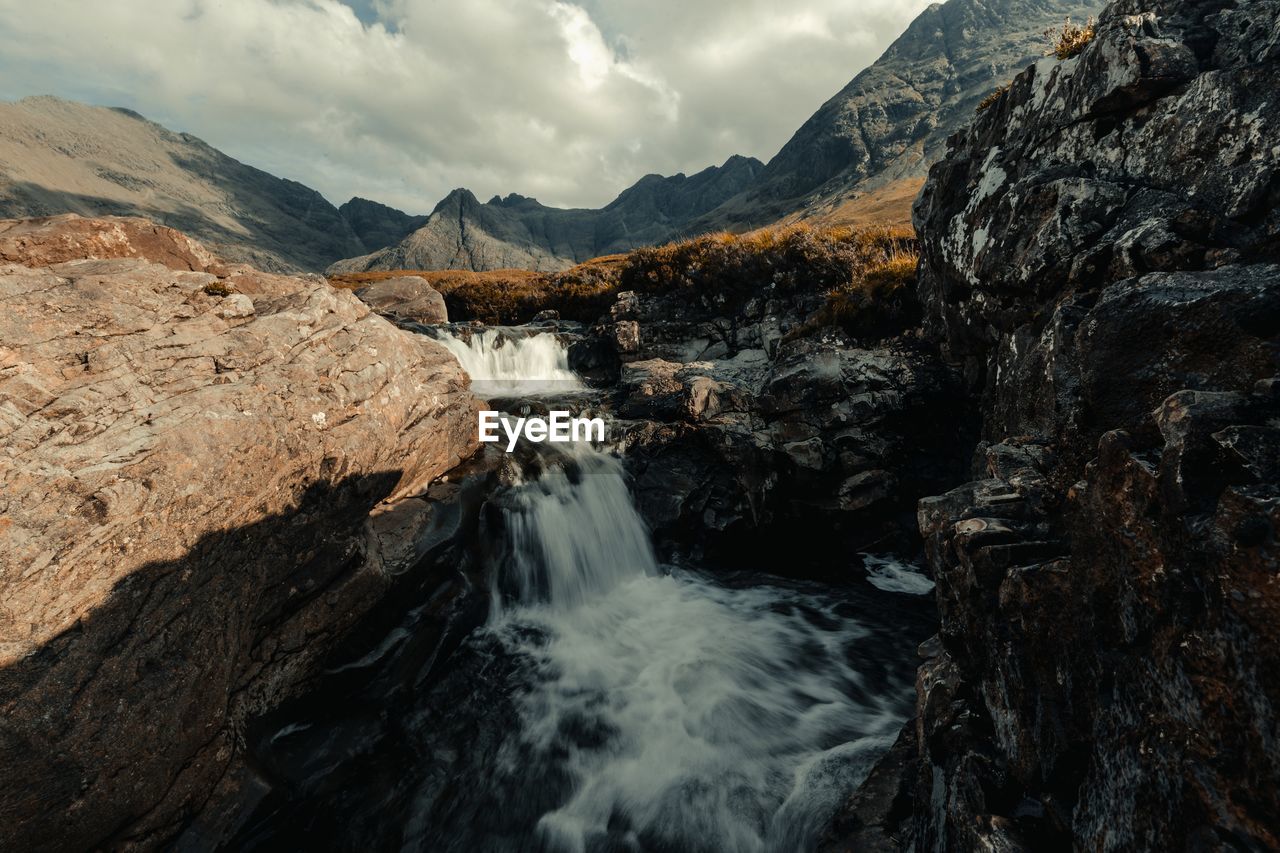 Scenic view of waterfall and mountains against cloudy sky