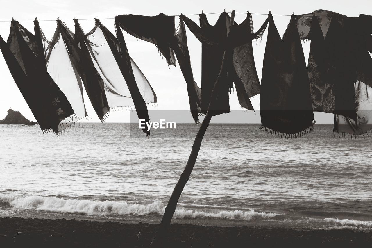 Clothes drying on clothesline at beach against sky