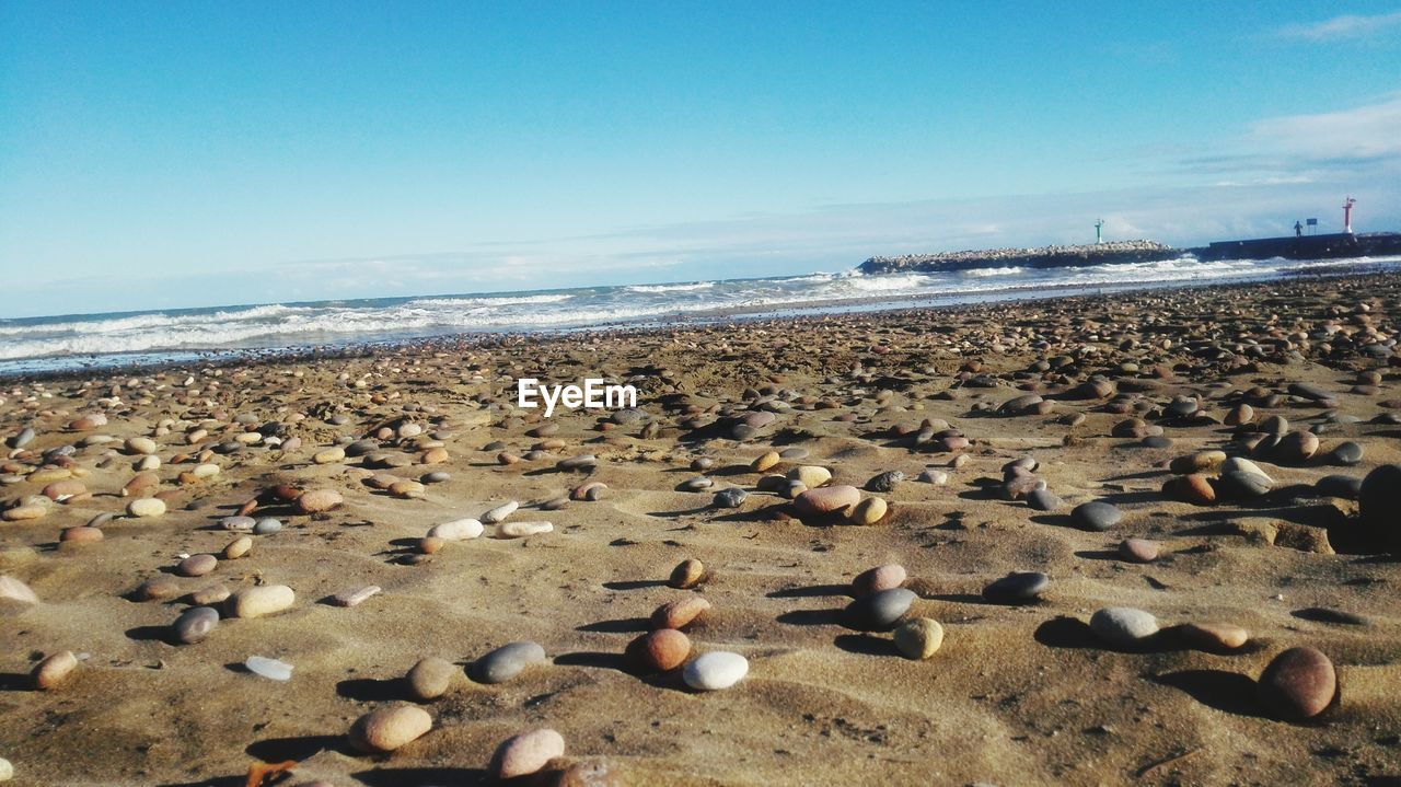 Pebbles at sandy beach against blue sky