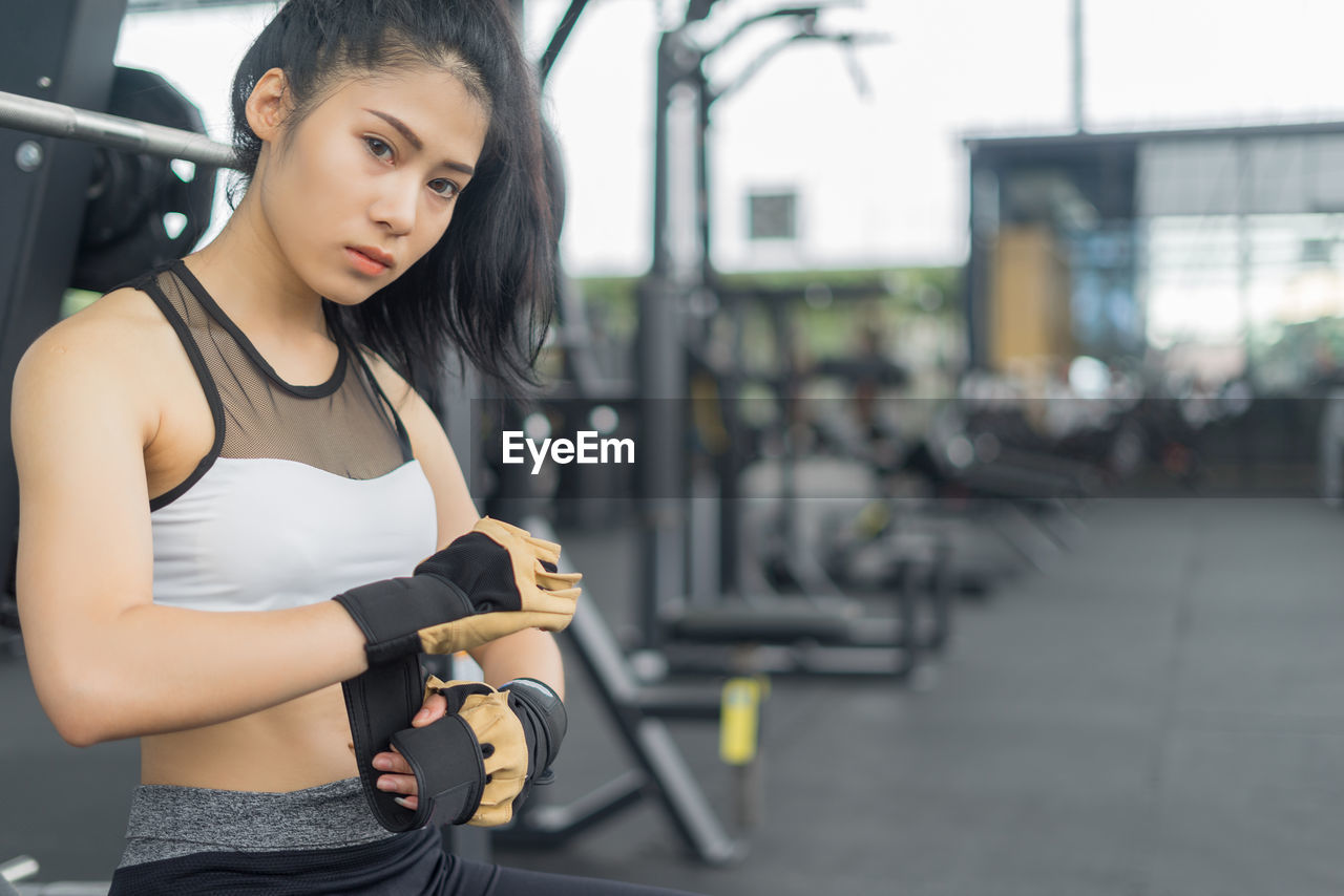 Young woman wearing glove while sitting at gym