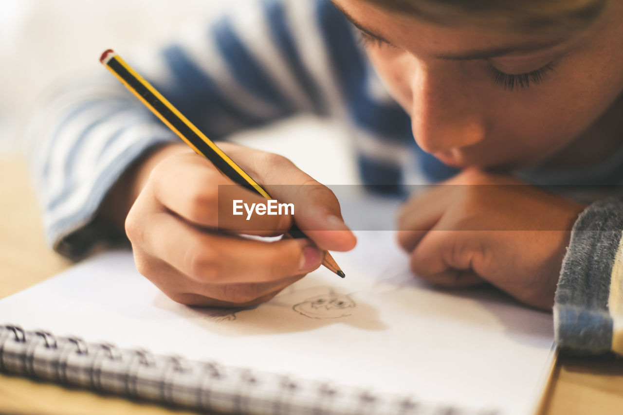 Midsection of boy making sketch on book while sitting at home