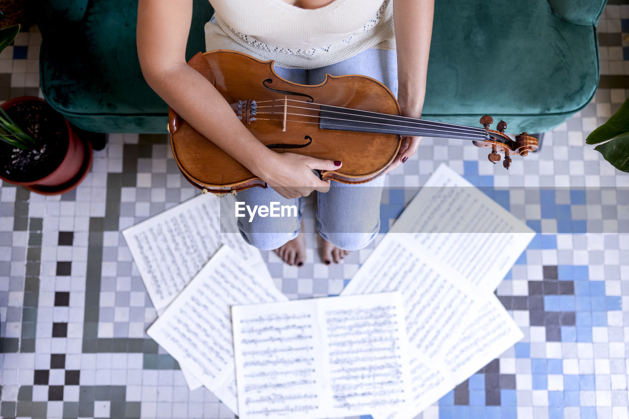 Sitting girl holding a viola, sheet music surrounding her bare feet.