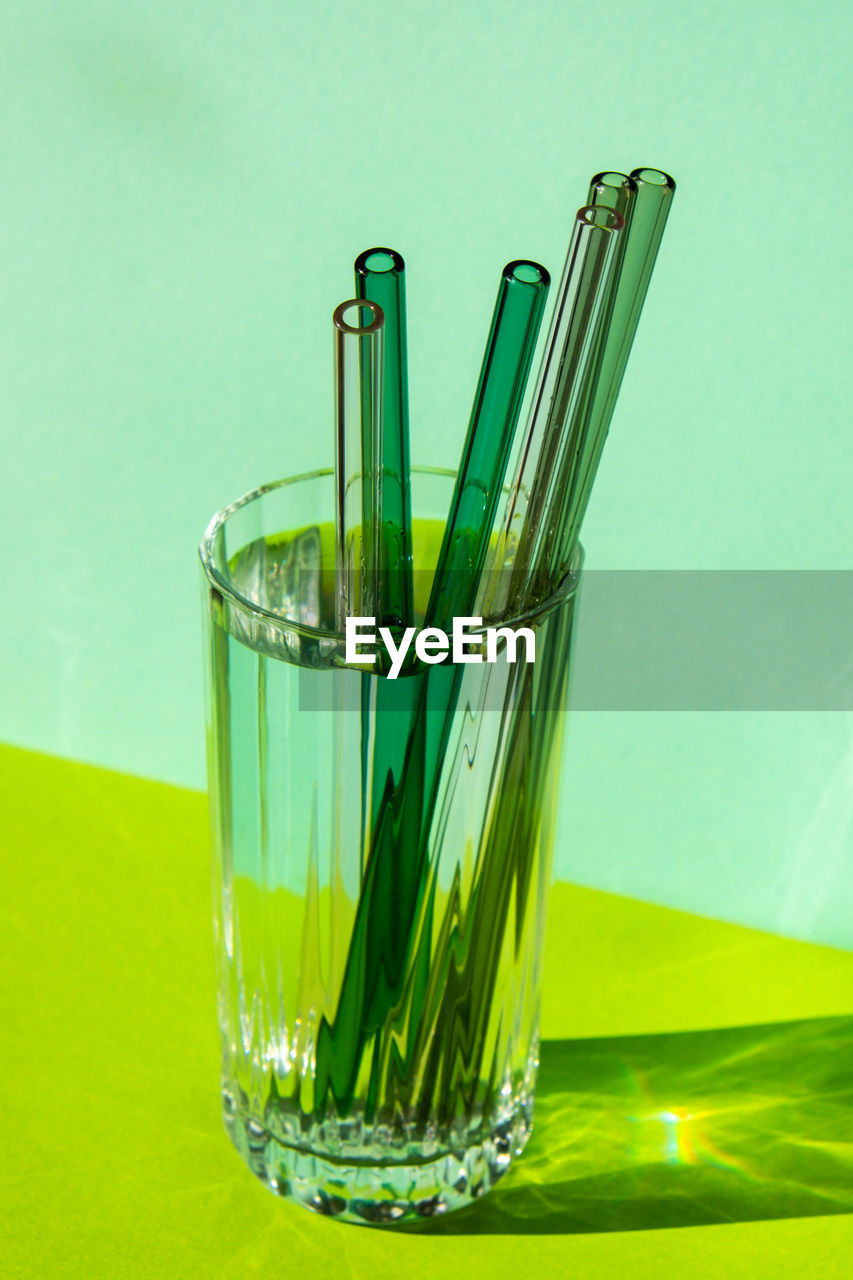 Reusable glass straws in glass with water on green background eco-friendly drinking straw set with