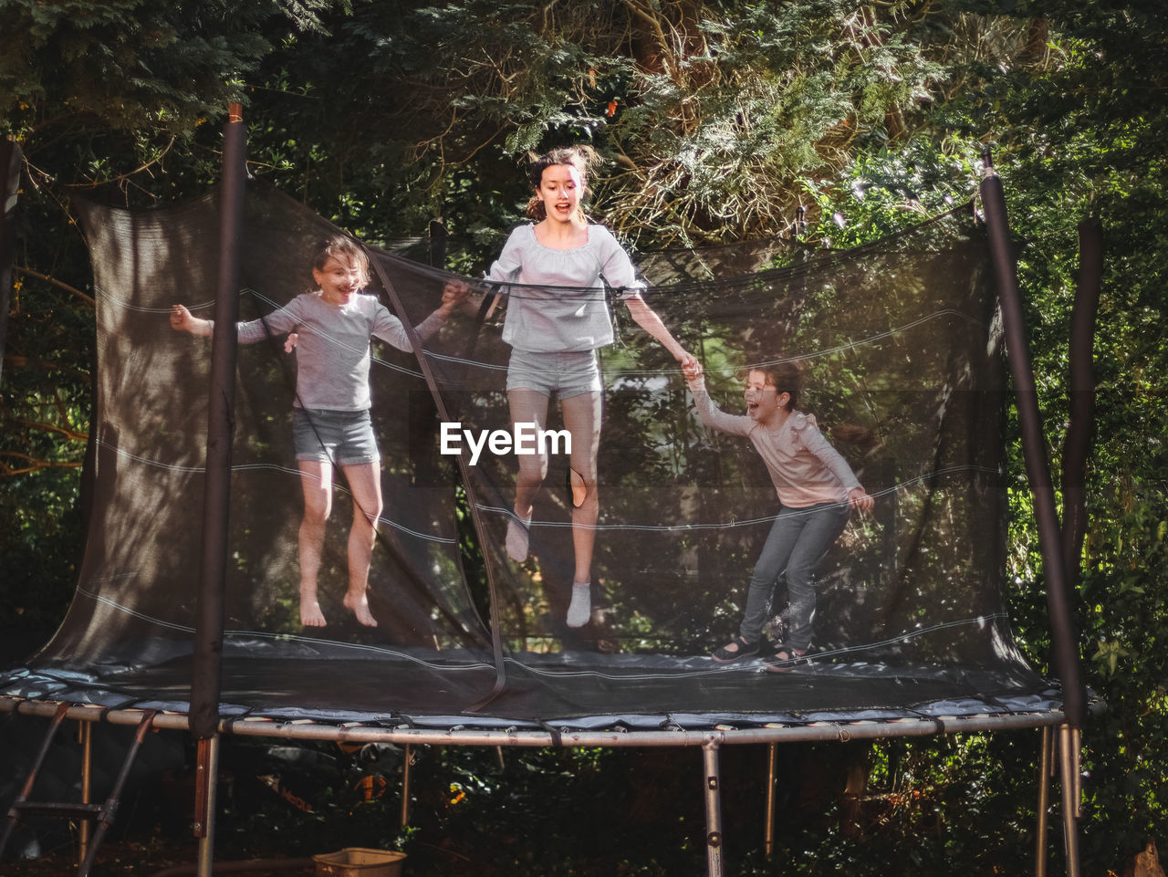 Three beautiful caucasian sister girls in jeans, shorts and a sleeved t-shirt jump on a trampoline