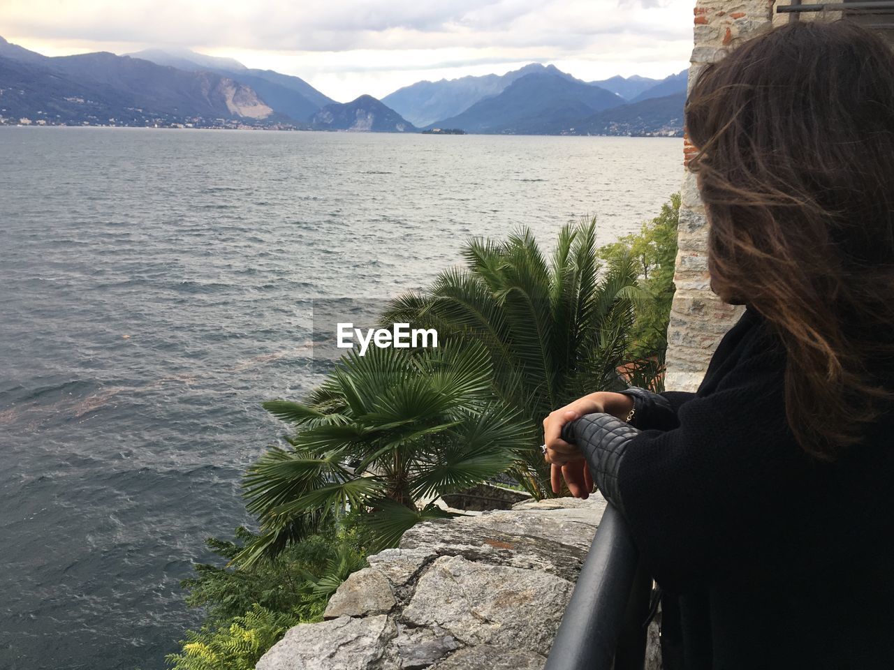 Side view of young woman standing by railing against lake