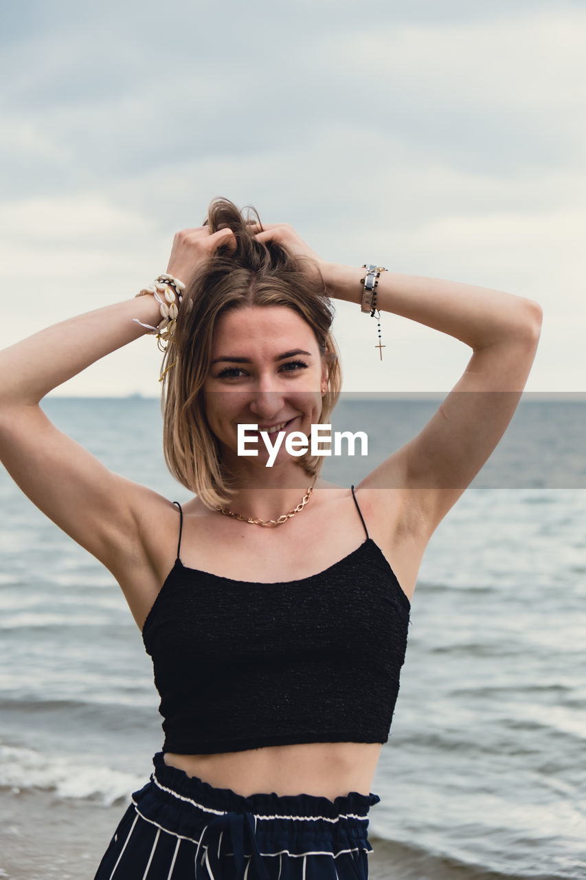 portrait of young woman standing against sea against sky