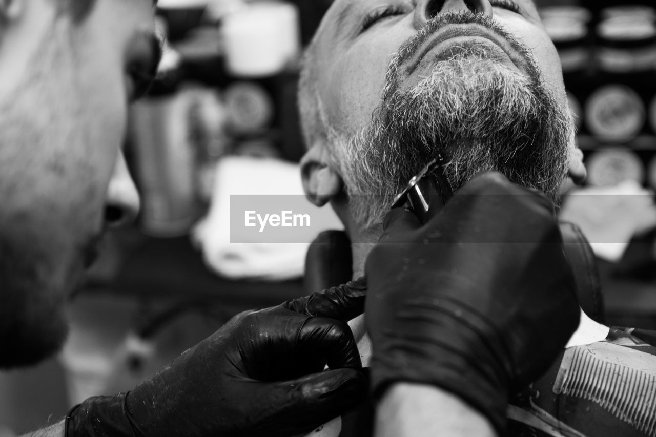 Barber trimming beard of man at salon