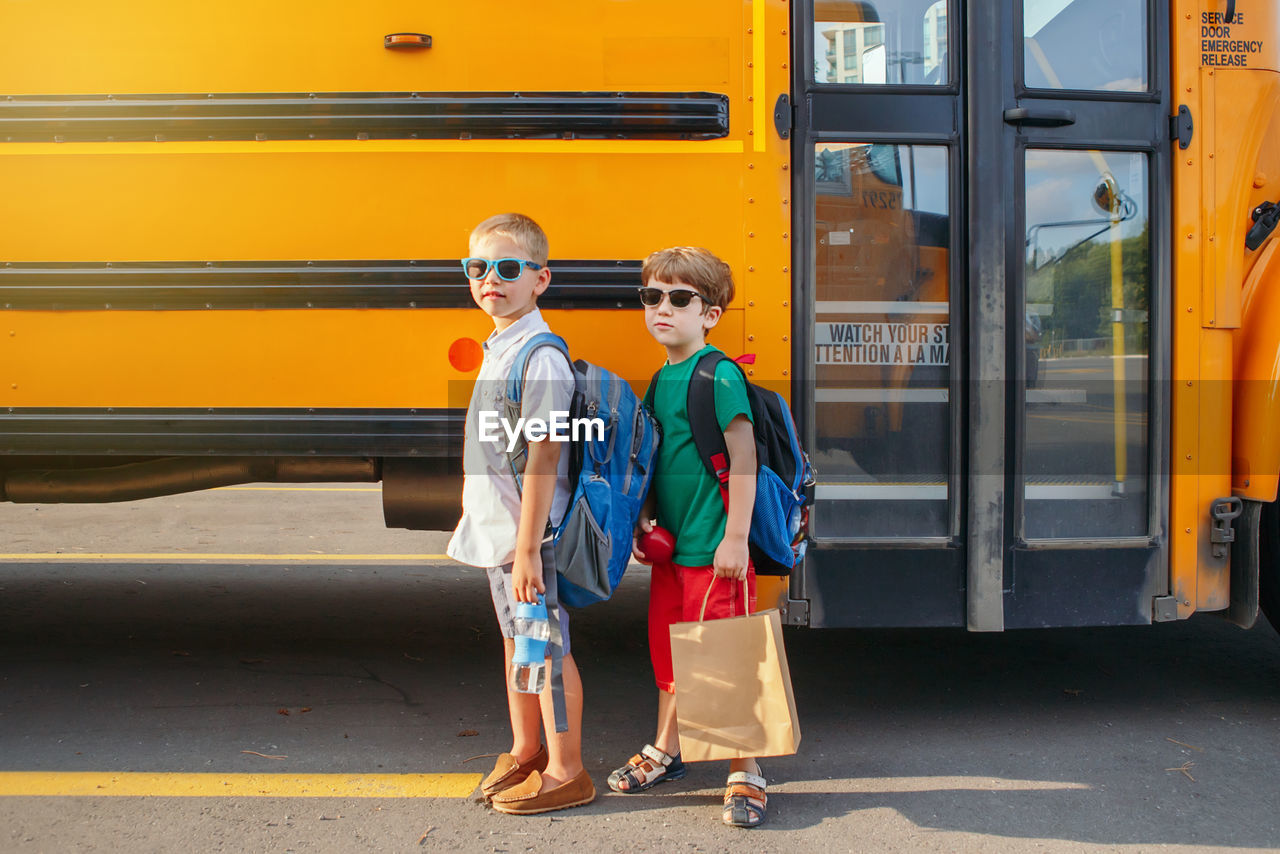 Full length portrait of boys while standing on road by bus