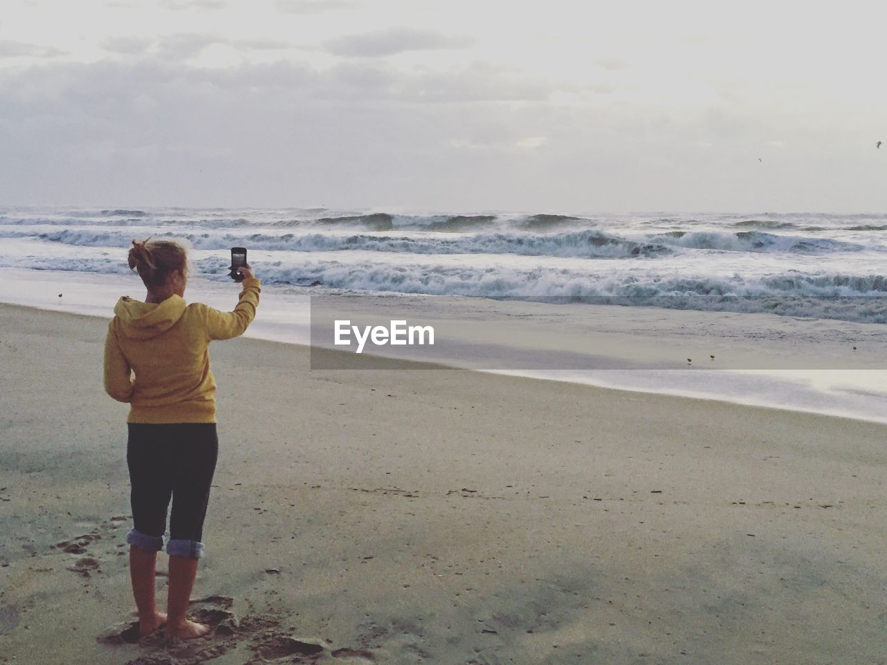 Rear view full length of woman photographing while standing at beach