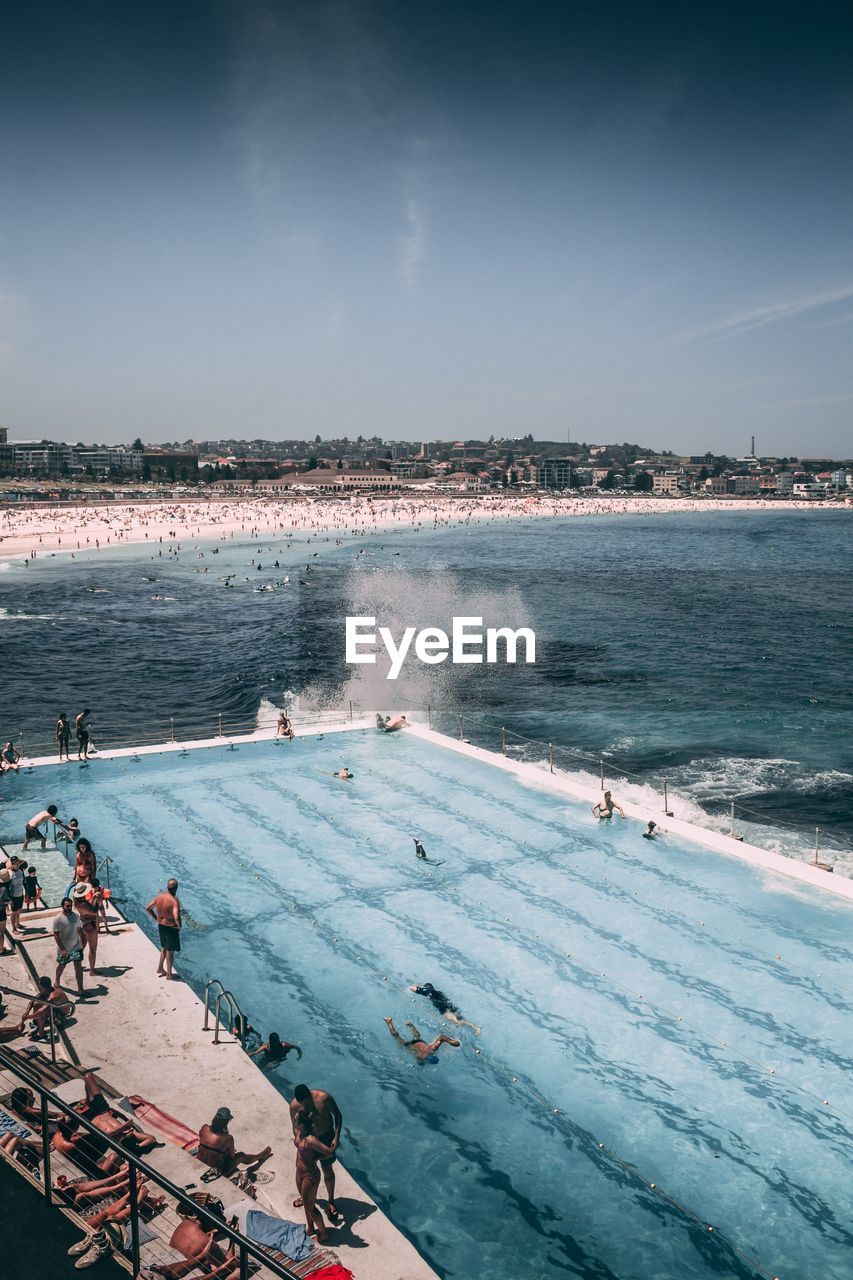 High angle view of people in swimming pool by sea against sky during sunny day