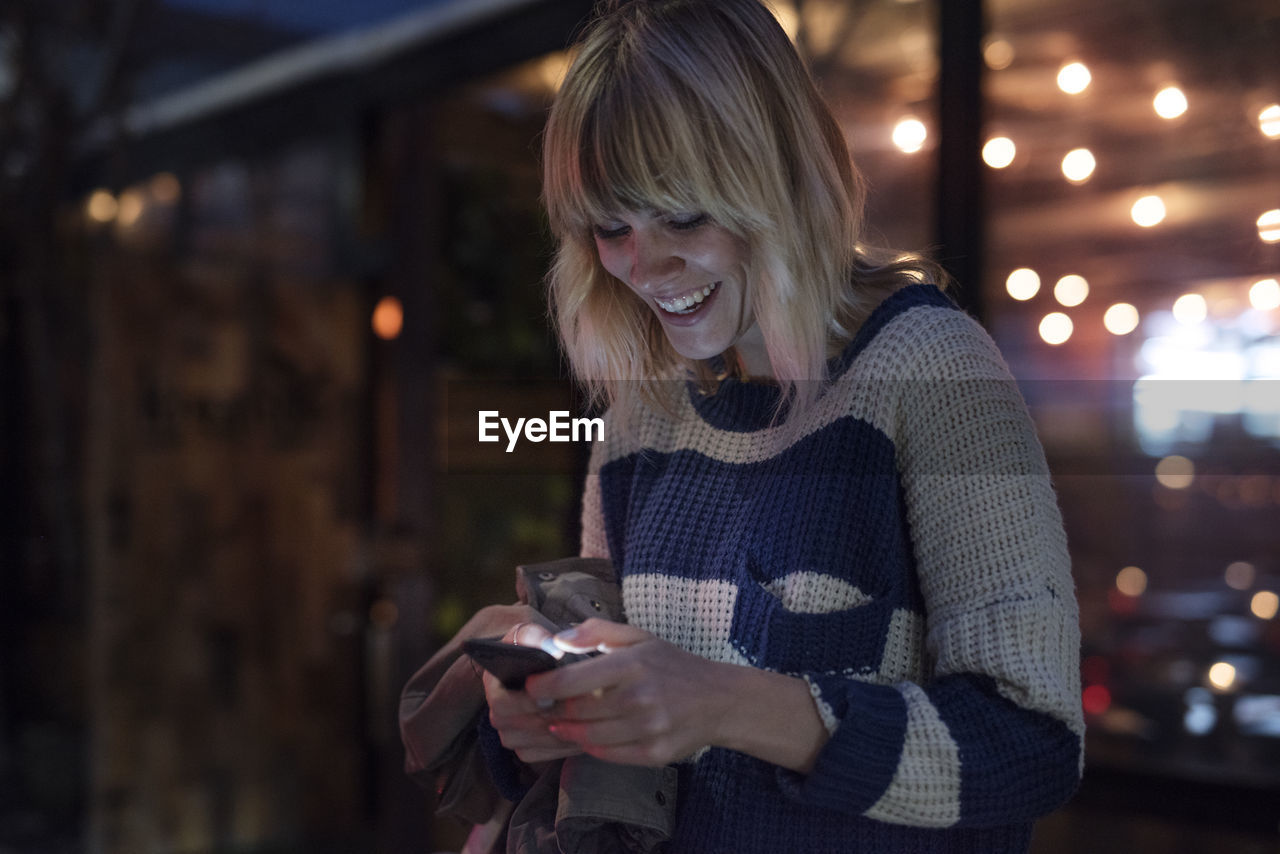Happy woman using smart phone in illuminated city at night