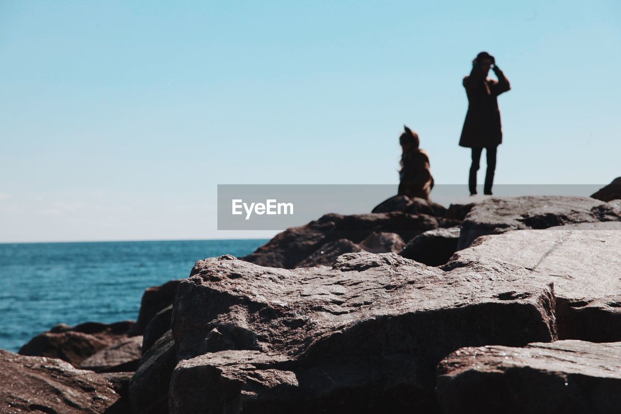 People standing on cliff by sea against clear sky