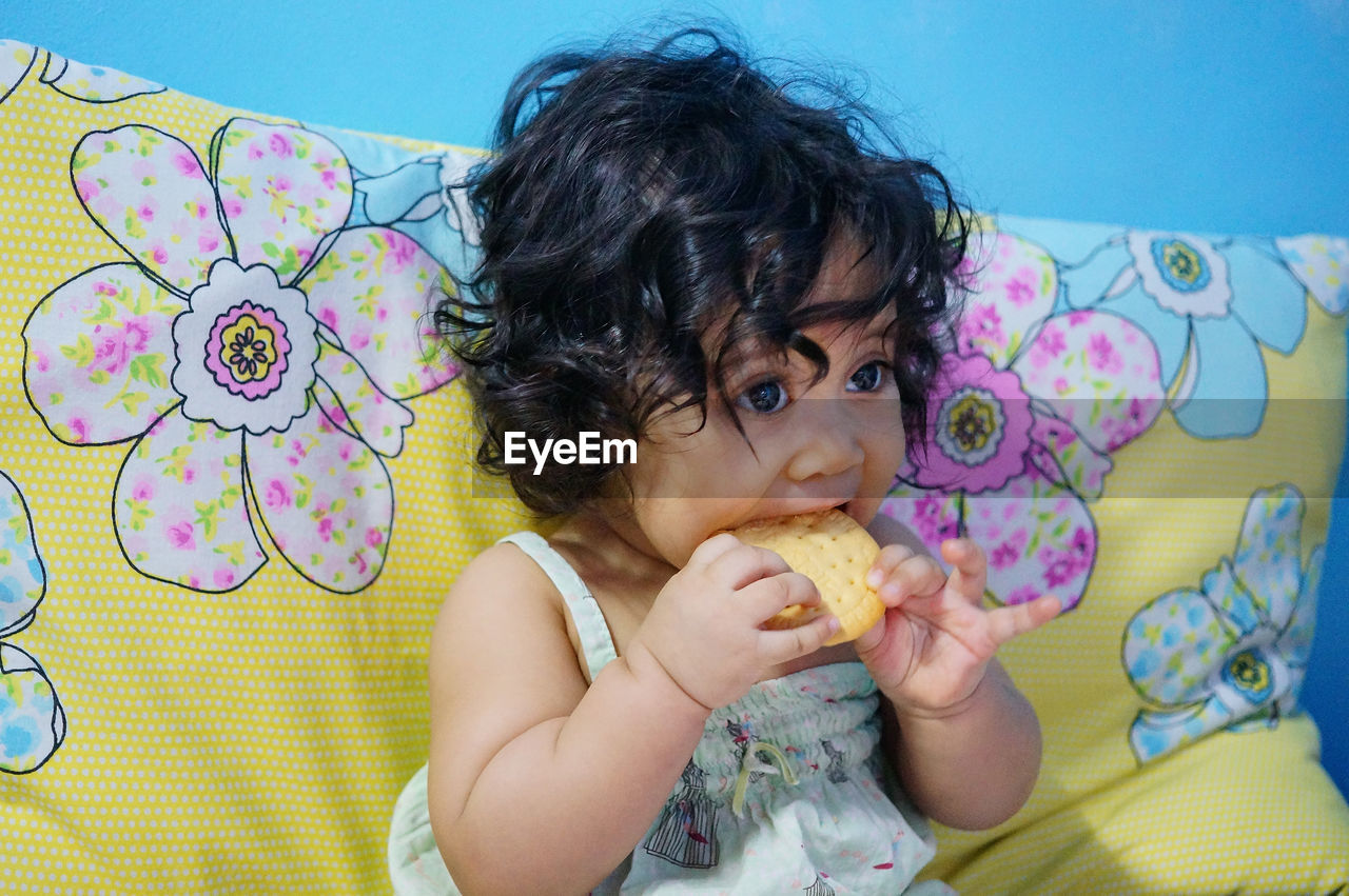 Close-up of cute baby girl eating biscuit while sitting on sofa