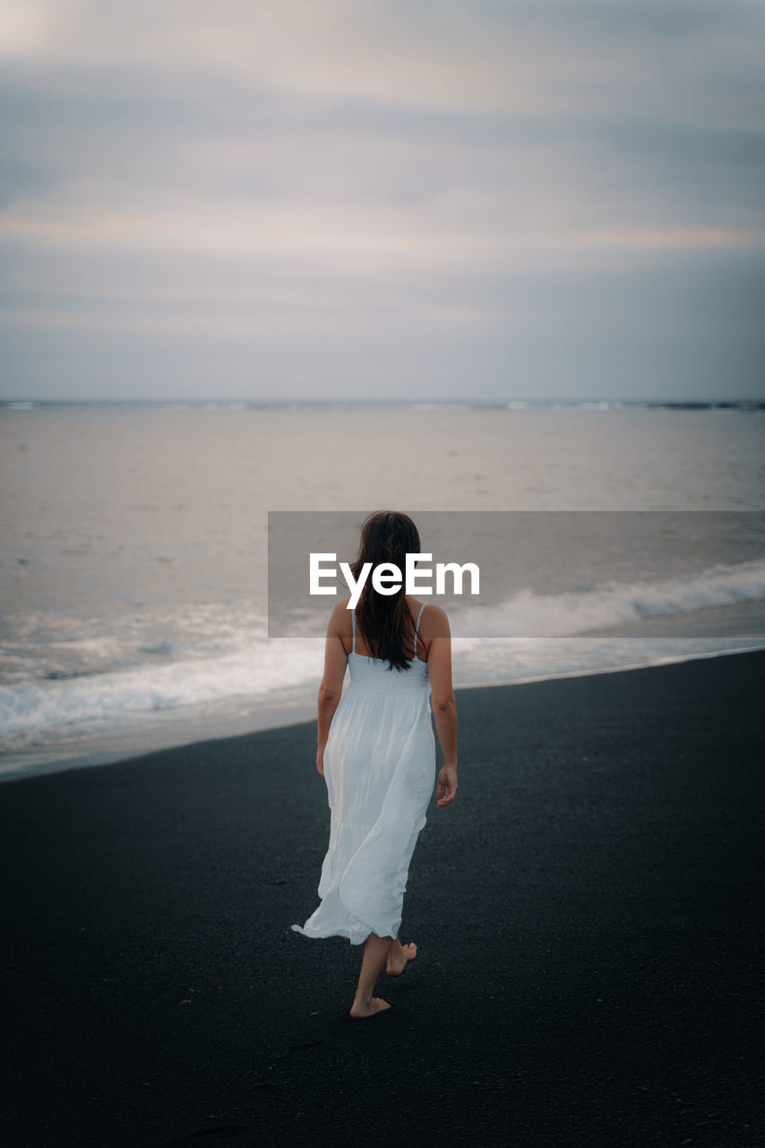 Rear view of woman walking on beach against sky