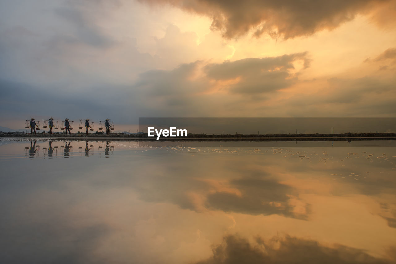 Scenic reflection view of salt making field against sky during sunrise