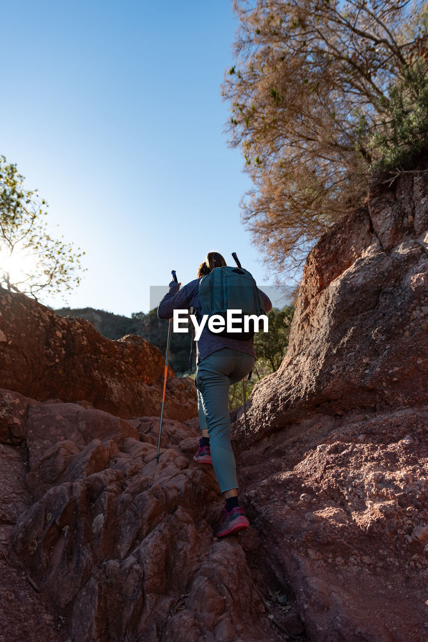 Woman climbs the mountain in the garraf natural park, supported by hiking sticks.