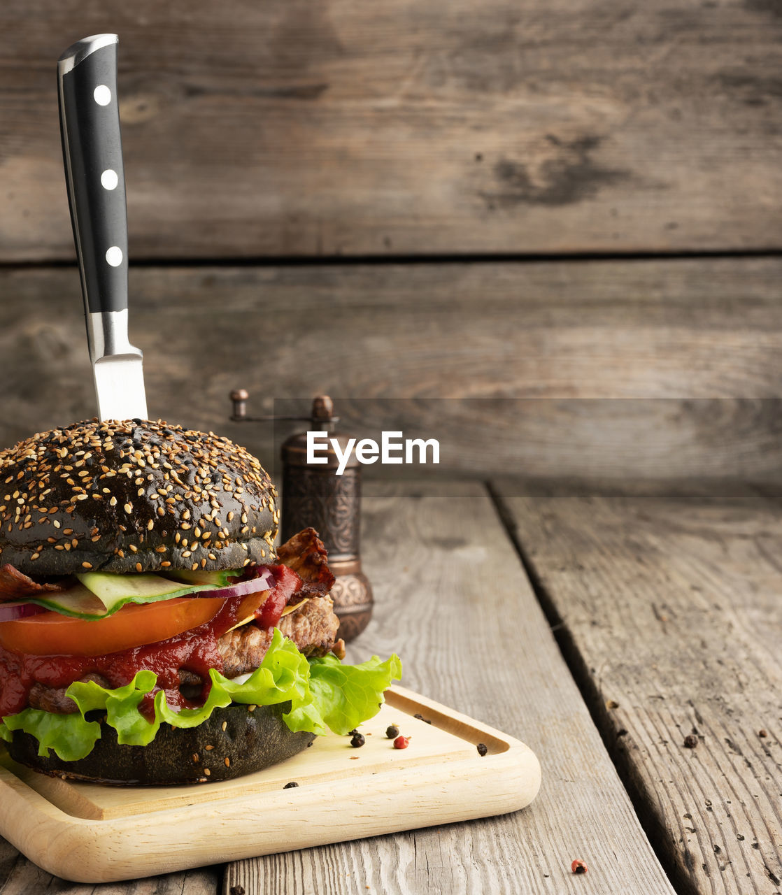 Cheeseburger with black bun, meat and vegetables on a wooden background, fast food