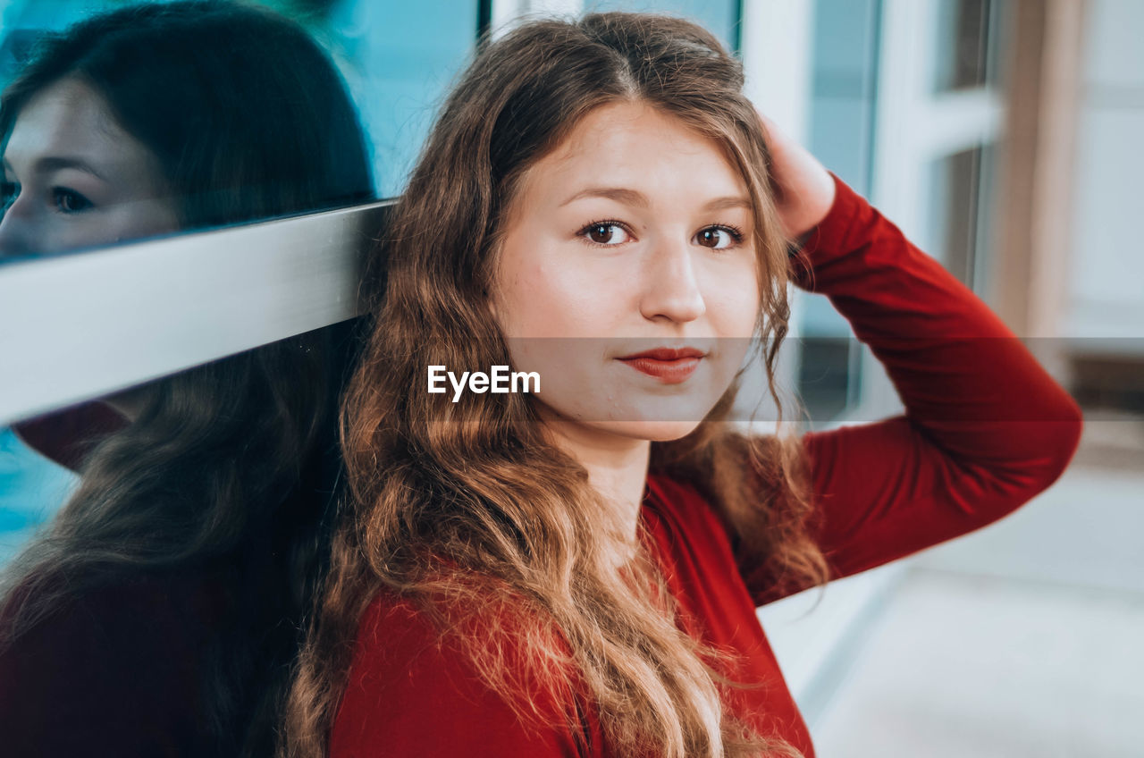 Close-up of beautiful girl sitting with hand in hair indoors