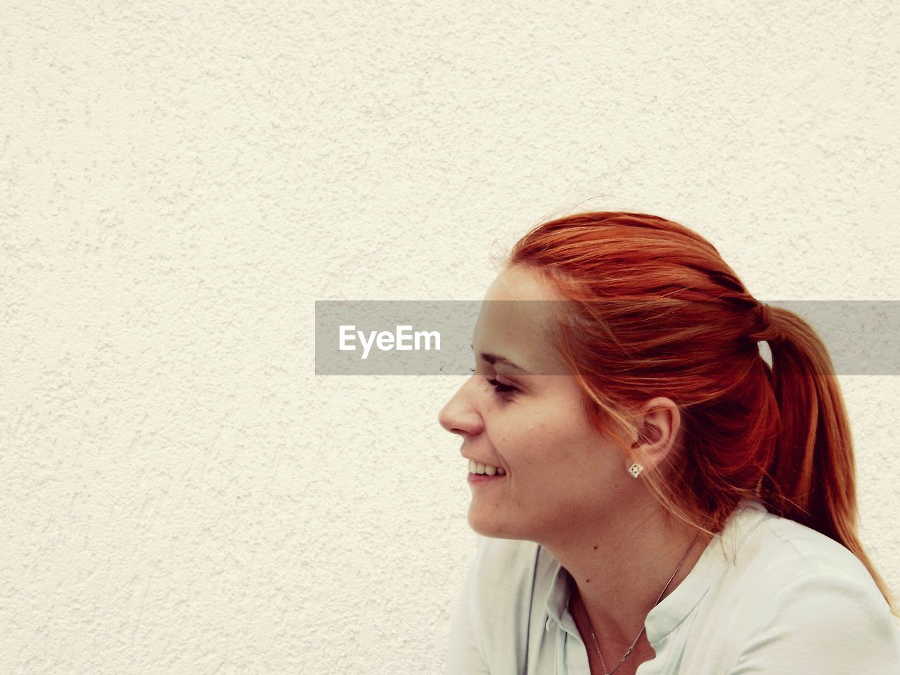 Close-up of smiling redhead woman by white wall