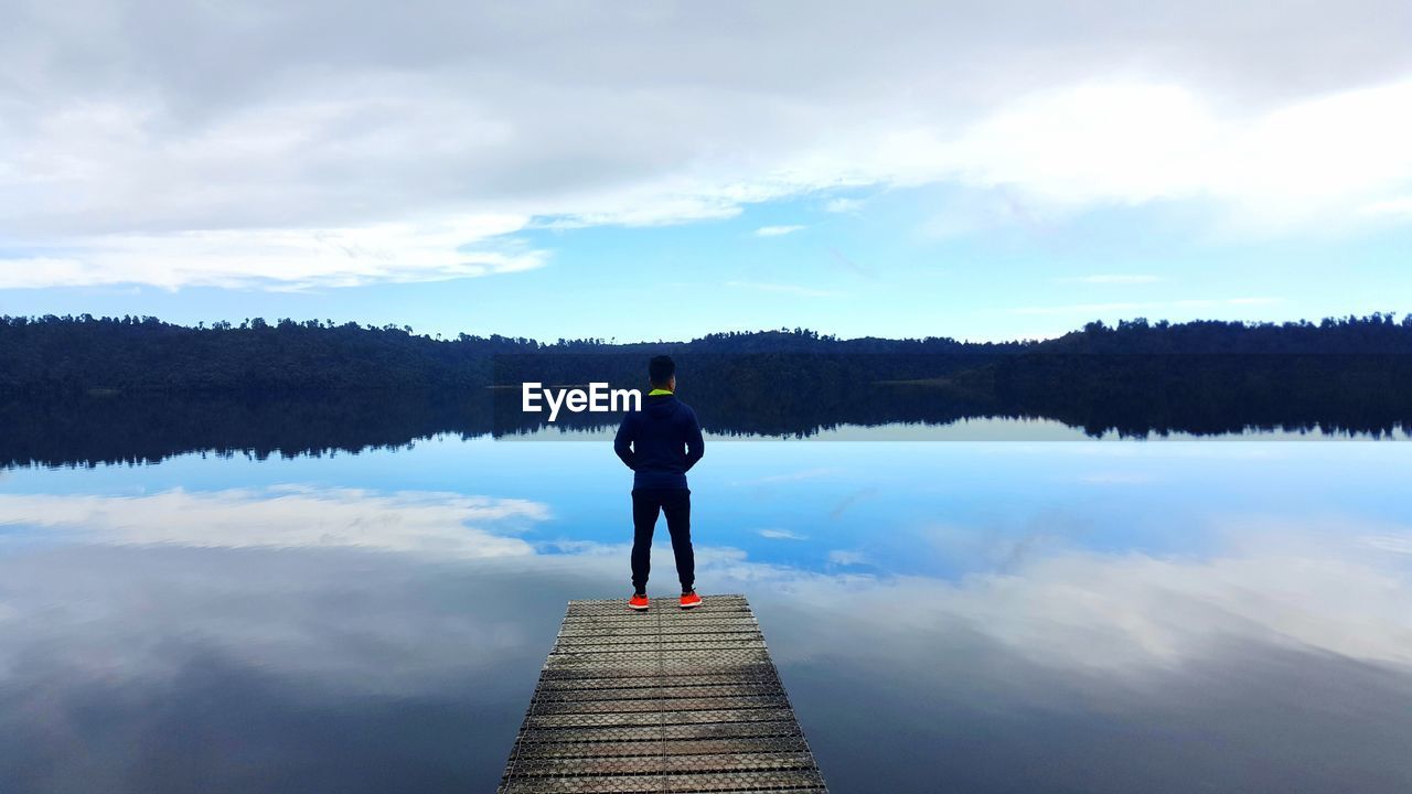 Rear view of man standing on jetty over lake against sky