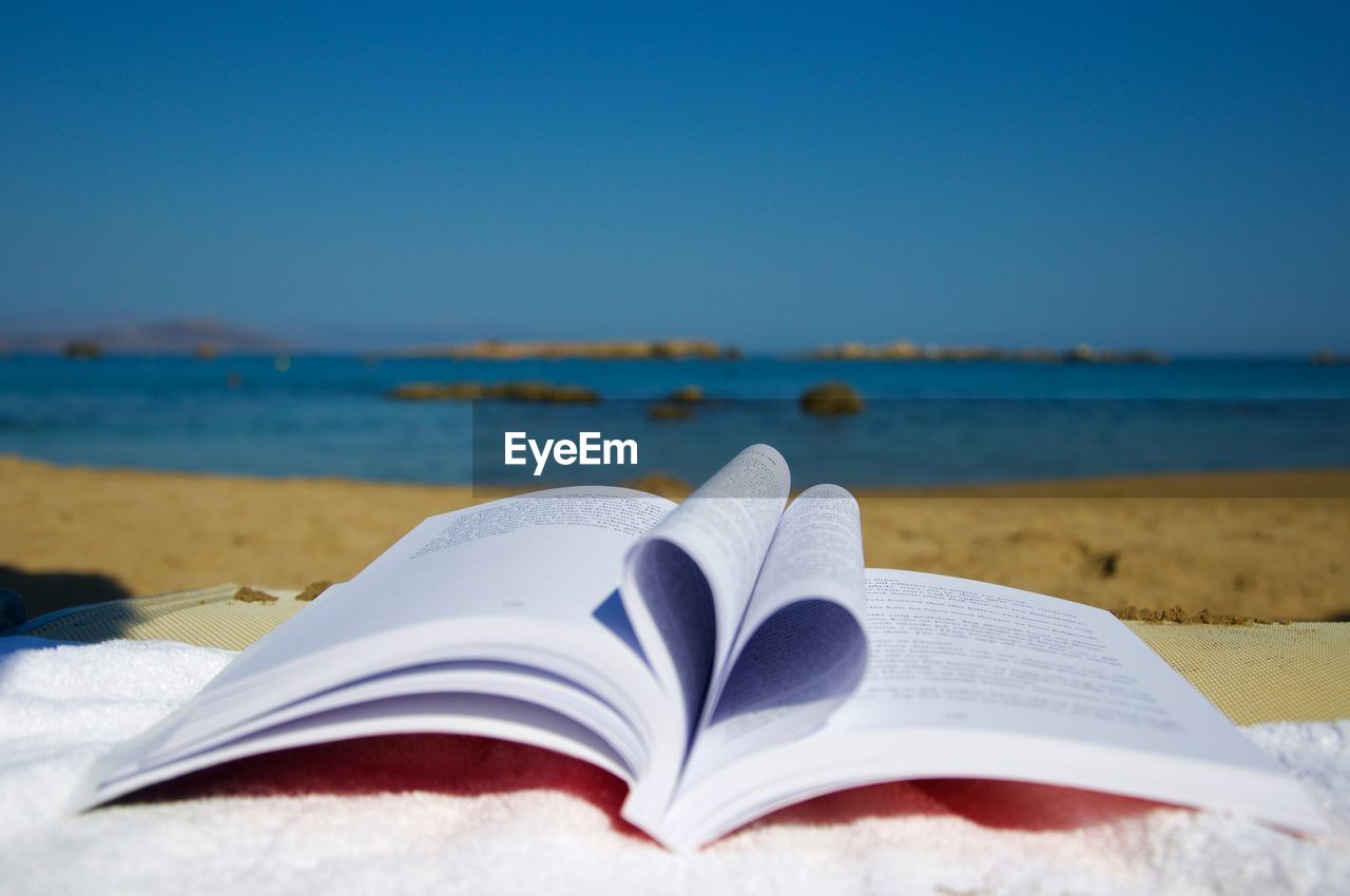 Close-up of open book on beach against blue sky