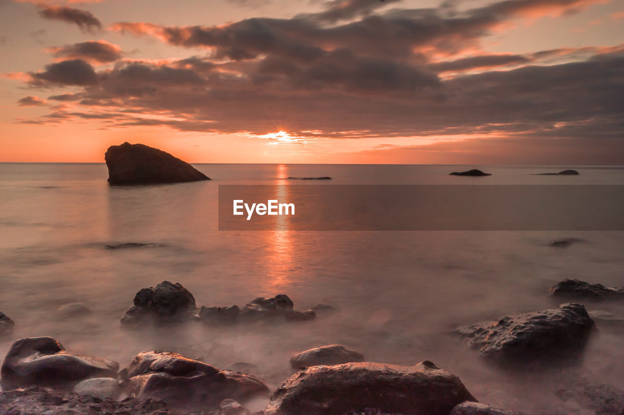 Scenic view of sea against cloudy sky during sunset