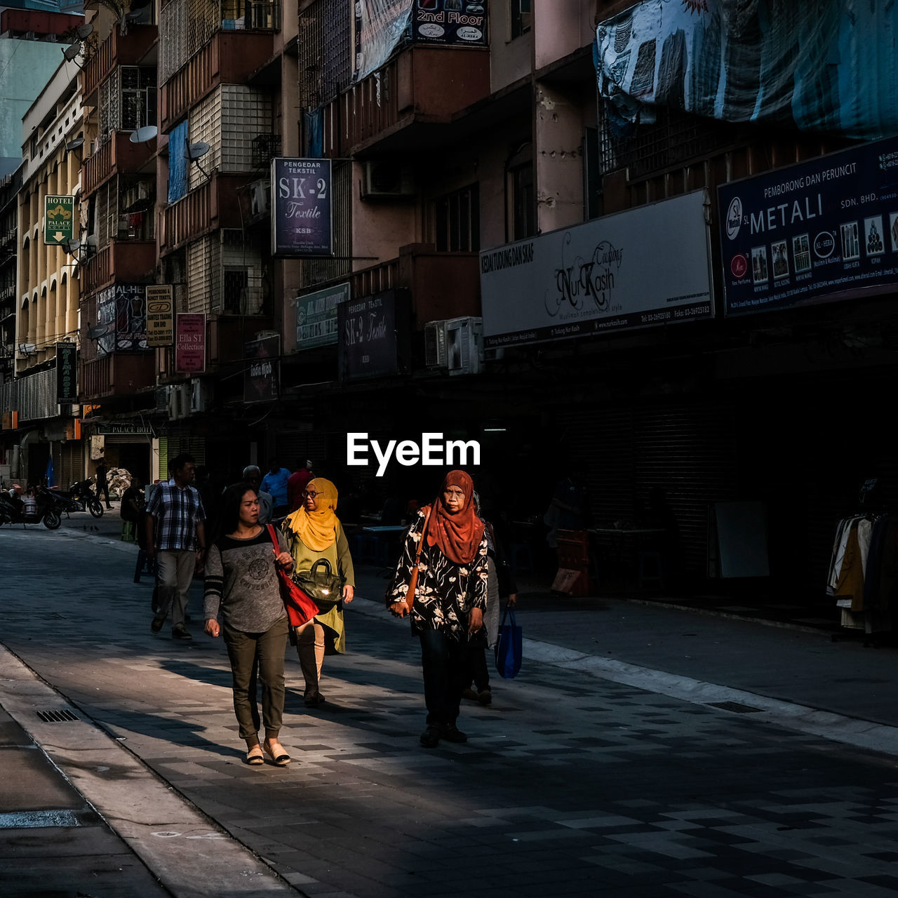 REAR VIEW OF PEOPLE WALKING ON STREET AMIDST BUILDINGS