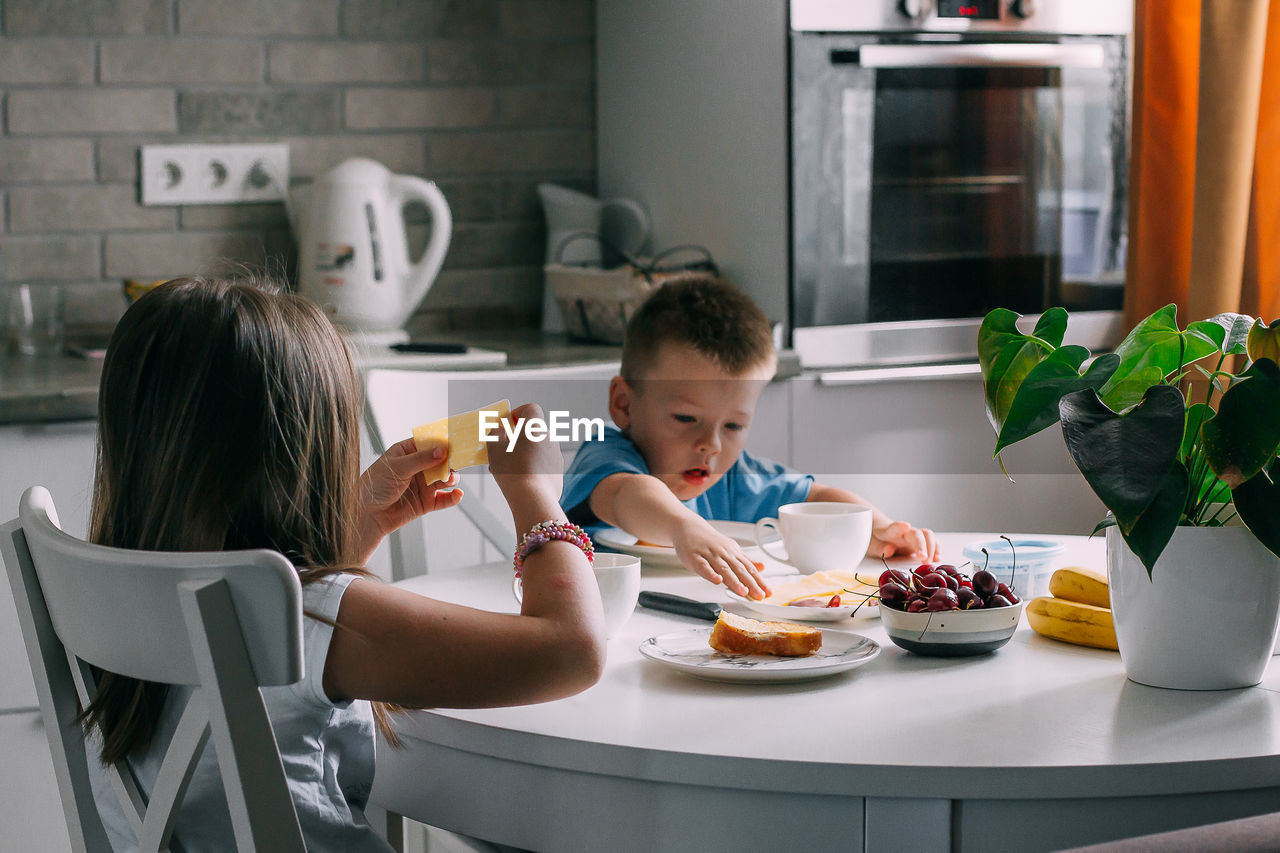 Sister and brother with food on table at home