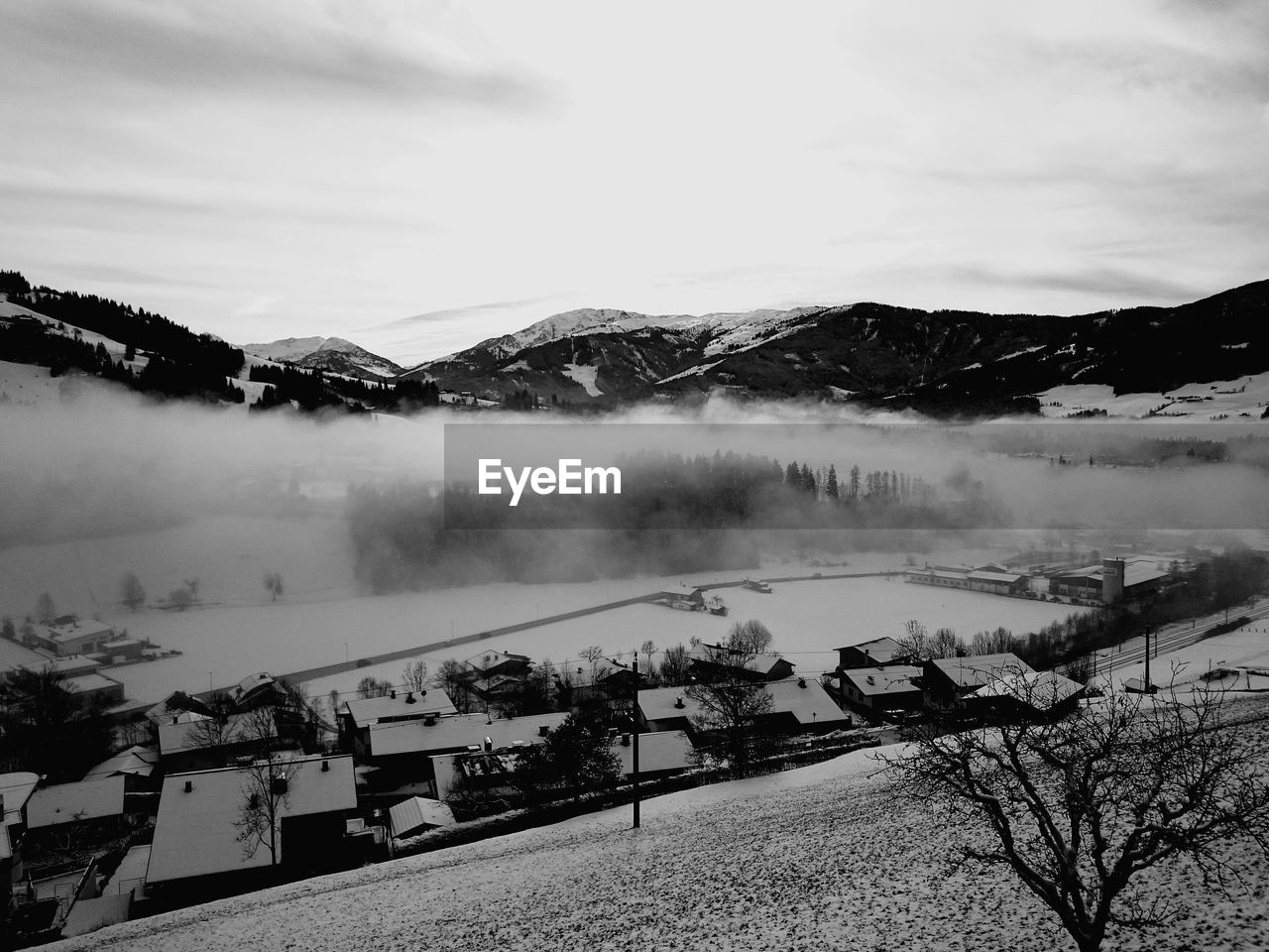 Fog over snow covered village against sky