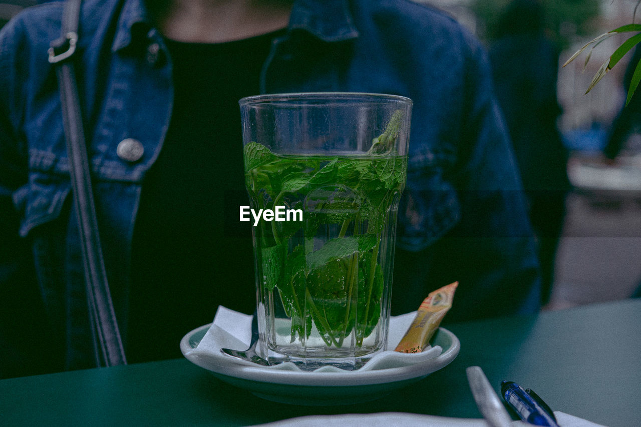 Close-up of drink in glass on table by woman