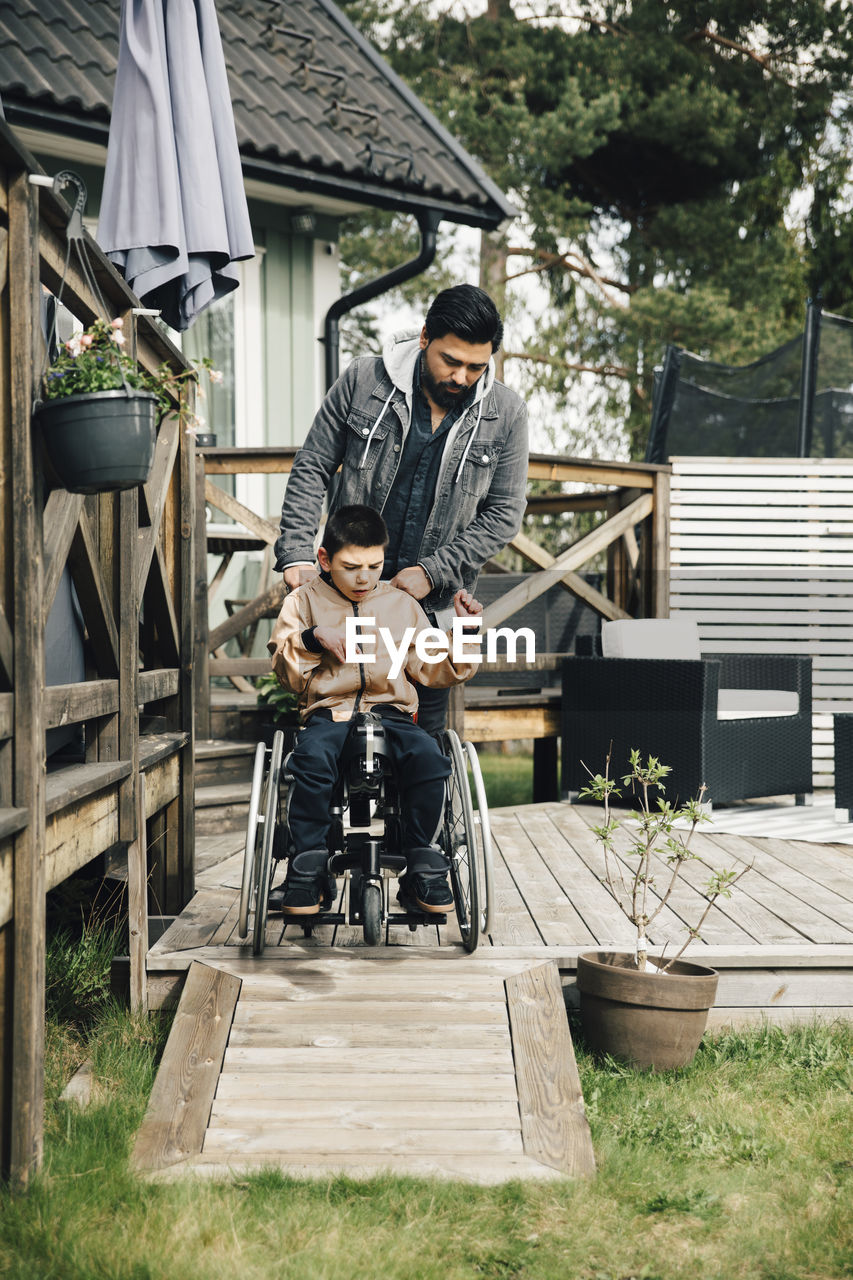 Father pushing autistic son sitting on wheelchair in yard