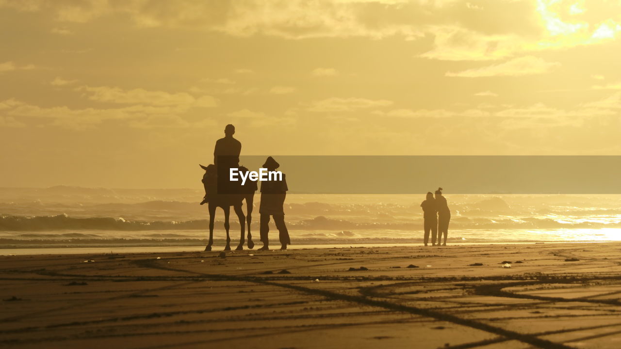 PEOPLE ON BEACH AGAINST SKY DURING SUNSET