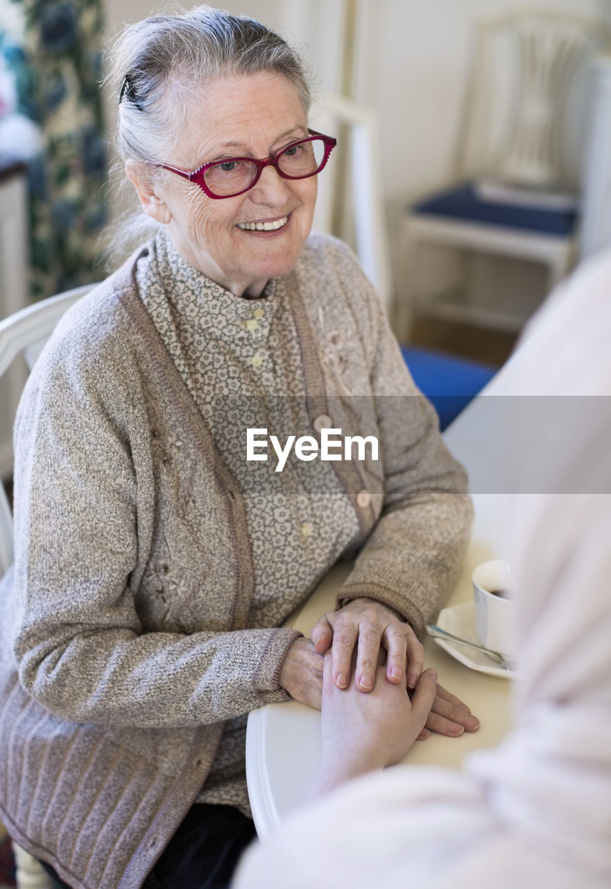 Smiling senior woman holding female home caregiver's hand at table