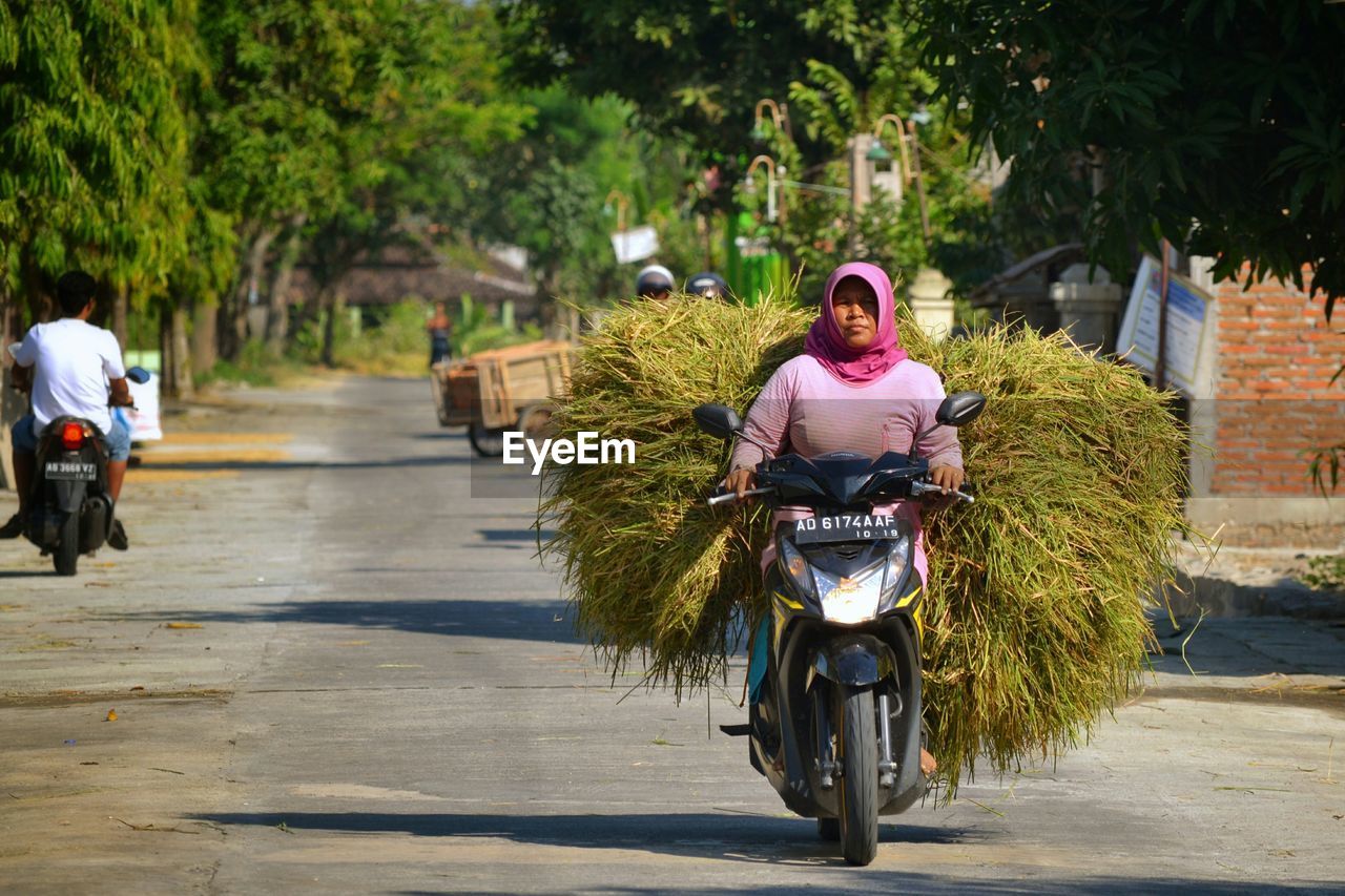 Woman carrying haystack on motor scooter