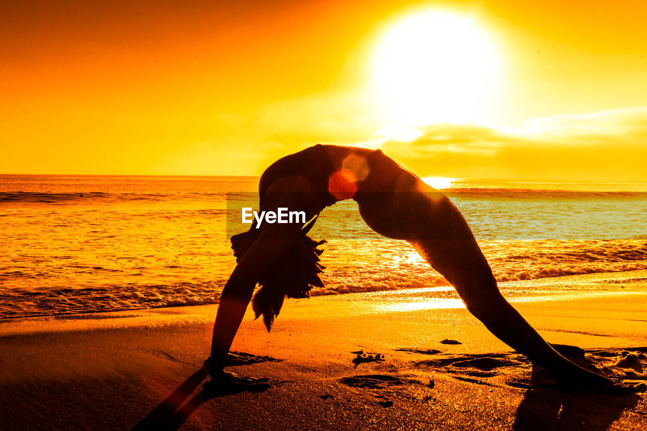 Woman exercising at beach during sunset