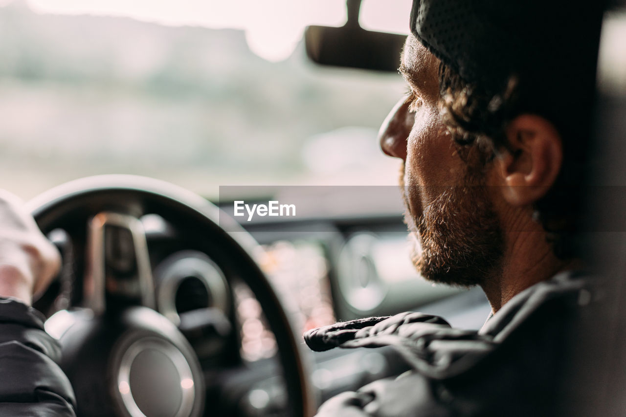 Side view of bearded man driving car on blurred background at sunset