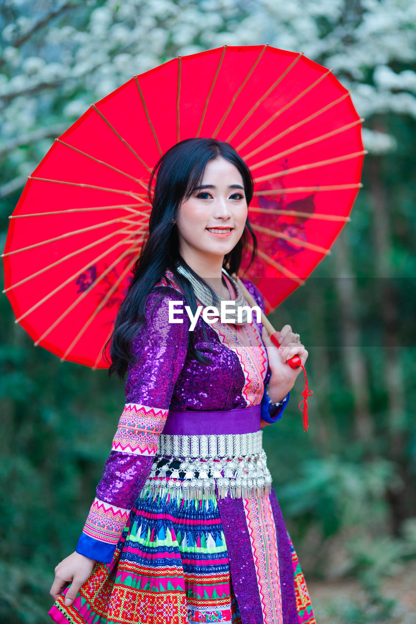 Portrait of smiling young woman with red umbrella standing outdoors