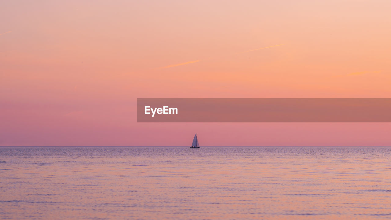 SAILBOAT SAILING IN SEA AGAINST SKY DURING SUNSET