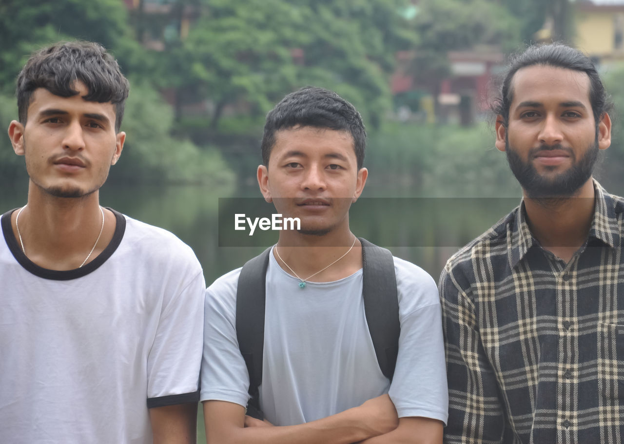 Closeup of three male friends looking at camera, posing for photo beside the lake