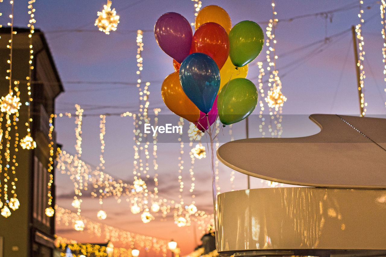 Low angle view of colorful balloons with illuminated lighting equipment hanging against sky at dusk