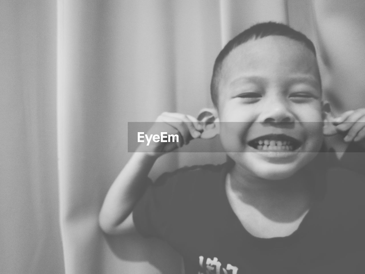 Close-up of cute boy pulling ears against curtain at home