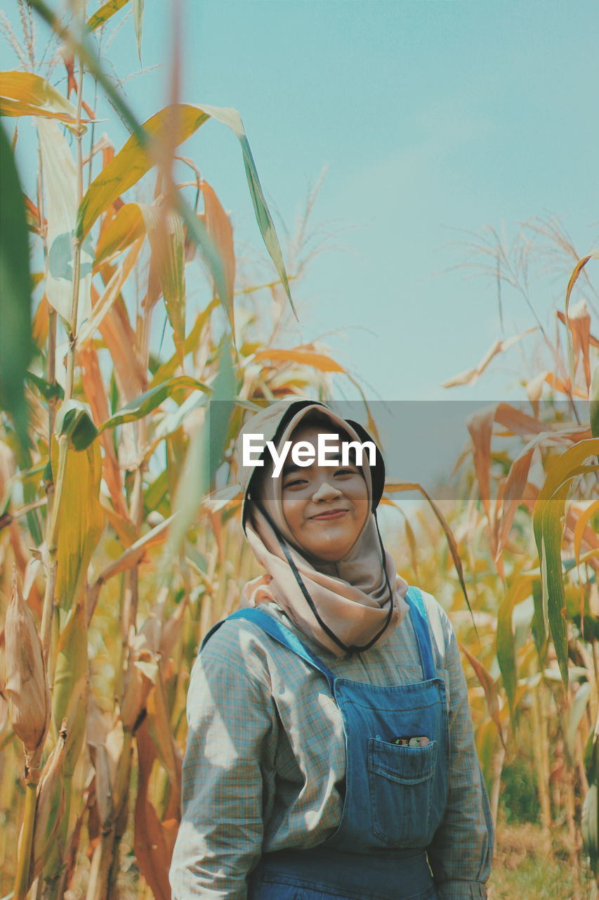 PORTRAIT OF SMILING WOMAN STANDING ON FIELD