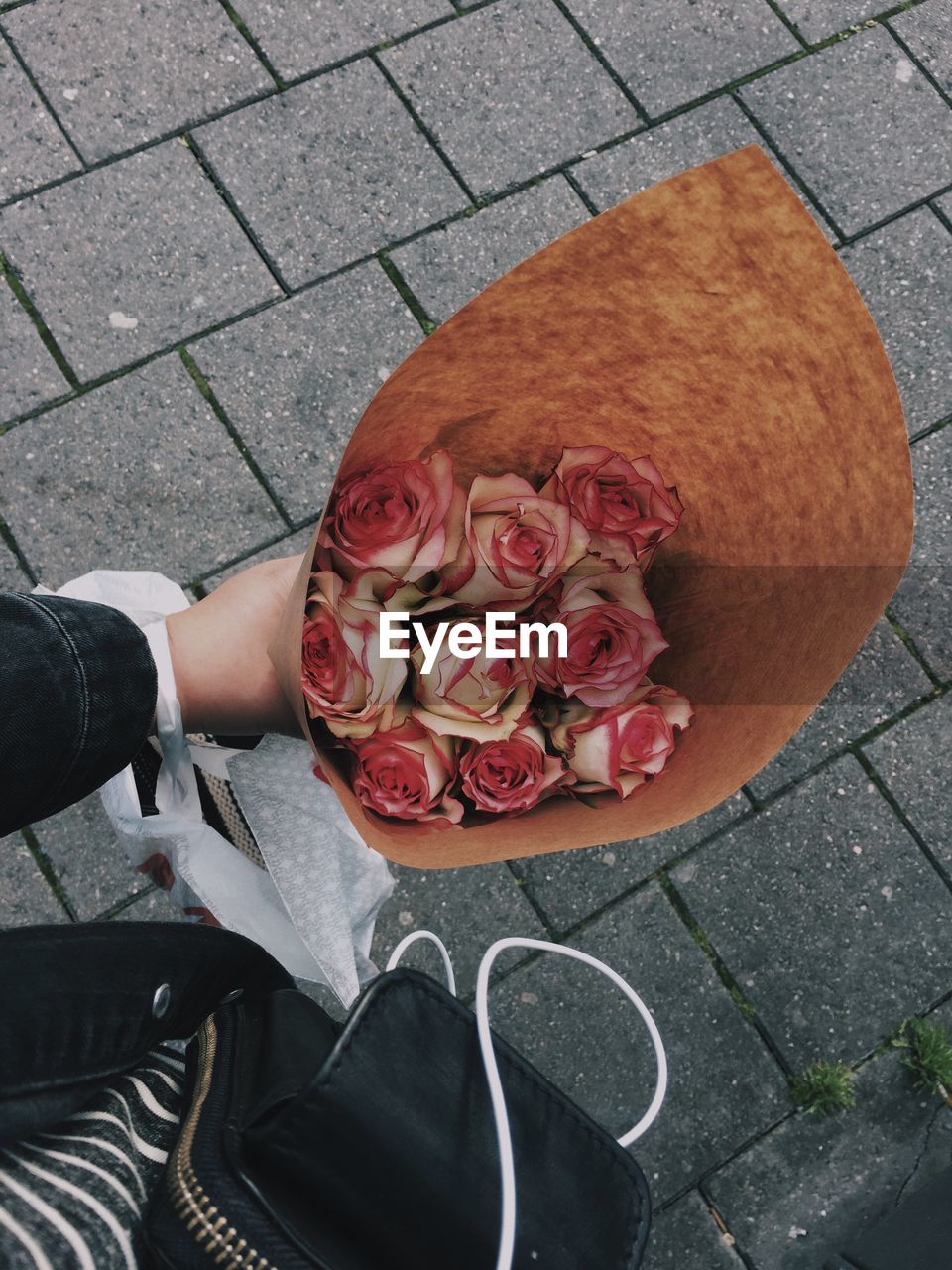 Cropped image of person holding rose bouquet on paved footpath