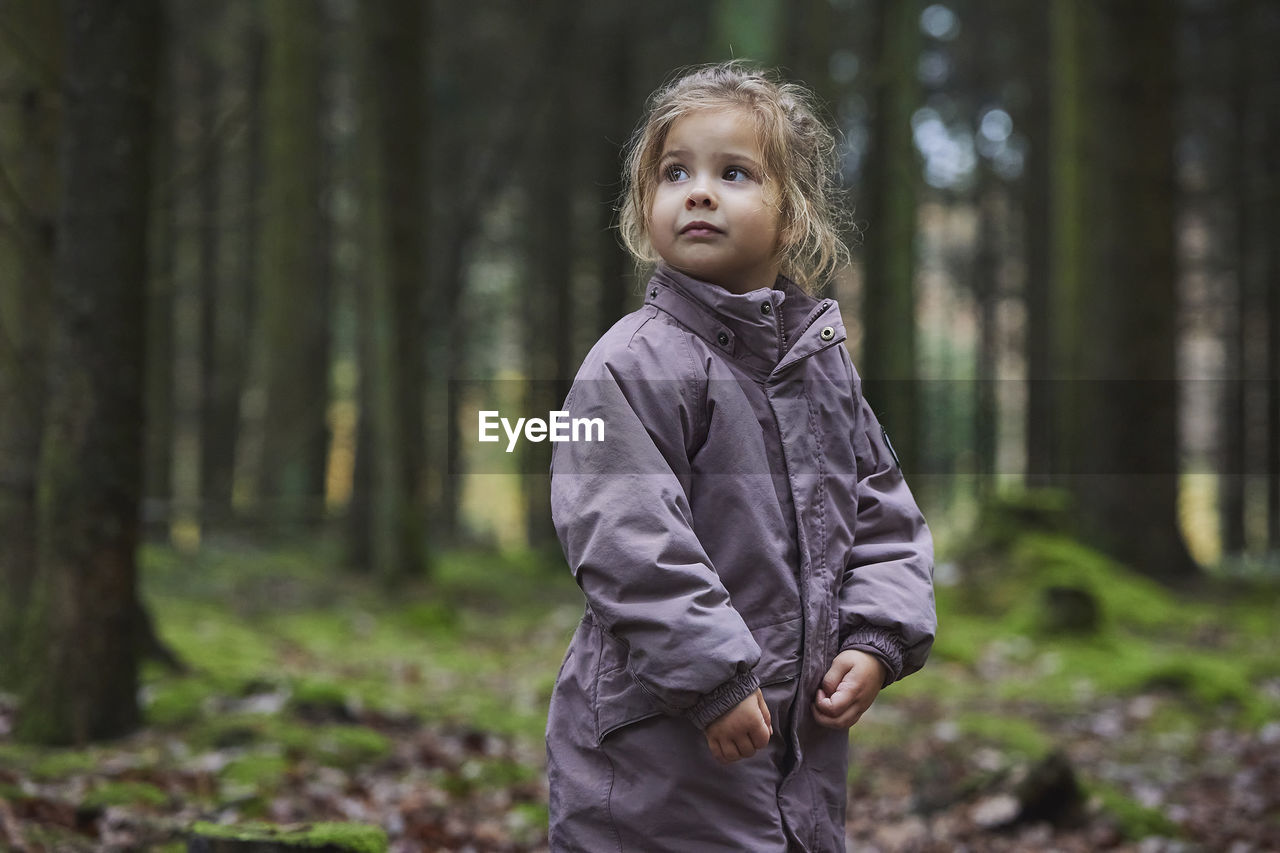 portrait of young woman standing against trees in forest